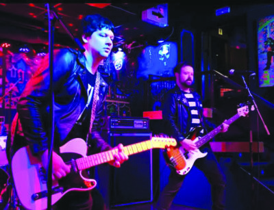 two men with guitars on stage under colors lights