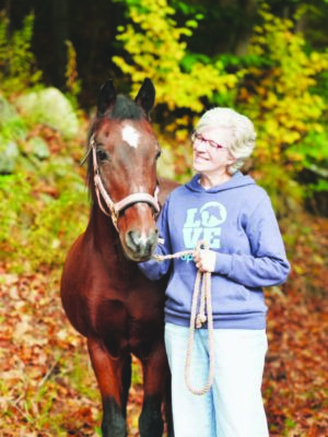 elderly woman standing with small horse outside on autumn day