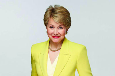 mature woman wearing light yellow blazer, short hair, closed mouth smile