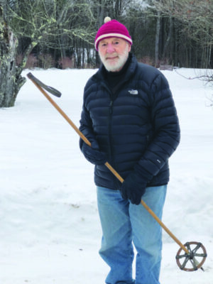 elderly man wearing warm winter hat, winter coat, standing outside in snowy lawn, holding old ski poll