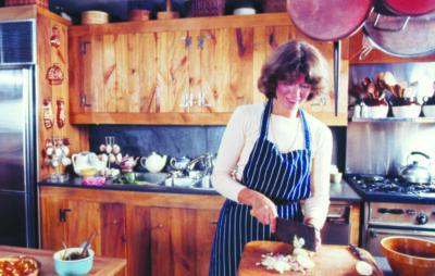 still from Martha Stewart documentary showing young Martha Stewart in kitchen with wooden cabinets, chopping onions