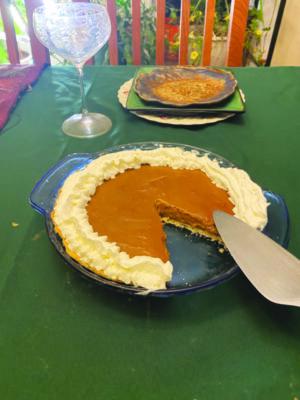 butterscotch pie with whipped cream around the edge, one triangular piece removed, on table in front of plate and wine glass