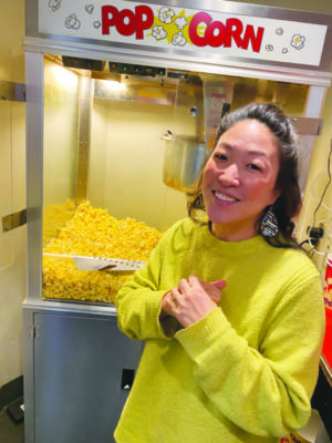 Asian woman standing in front of popcorn maker, smiling