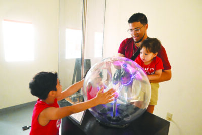 man with two small boys in science museum looking at ball of electricity