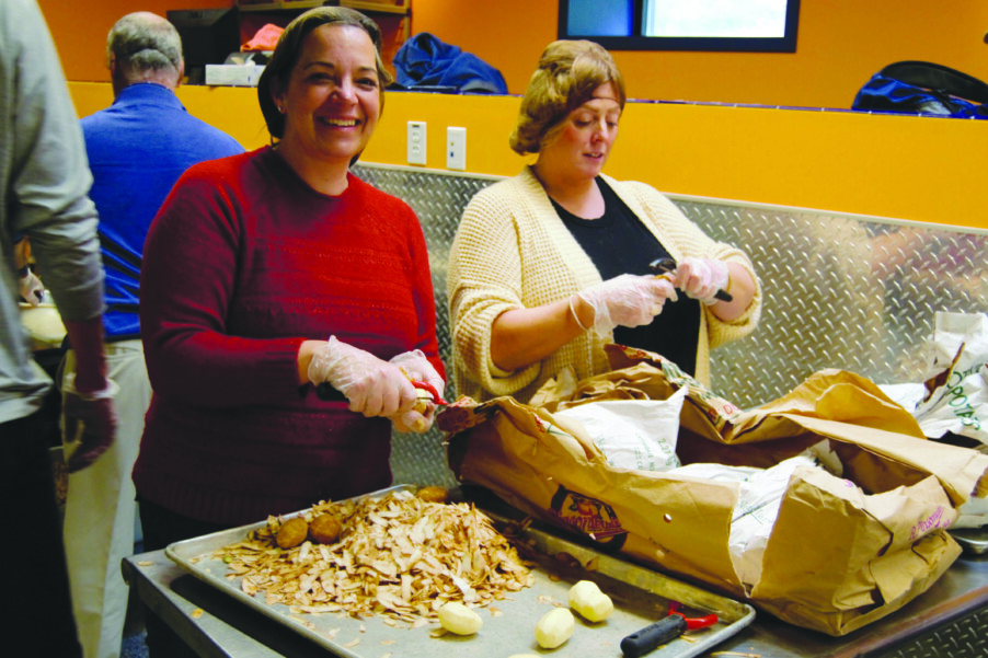 two women peeling bag of potatoes in industrial kitchen peelings on tray in front of them