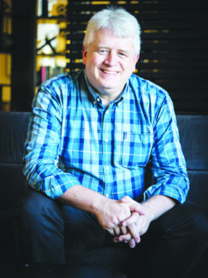 middle aged man with white hair, wearing blue plaid shirt, sitting on couch, portrait