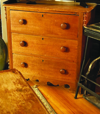 small three drawer wooden dresser sitting on hardwood floor, surrounded by other old items