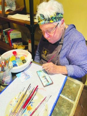 An elderly woman painting a snowy landscape onto a bar of chocolate