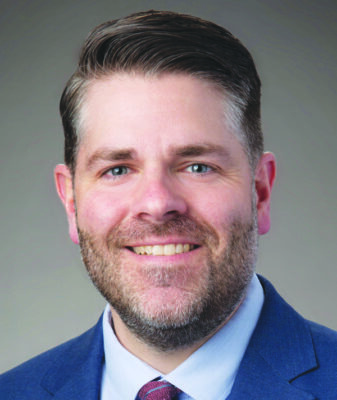 headshot of young-ish bearded man wearing suit and tie, smiling