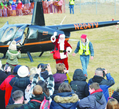 Santa arriving in helicopter in field, crowd of people waiting to greet him