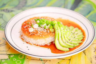 plate with round patty of white rice covered in orange sauce with sliced avocado arranged to the side