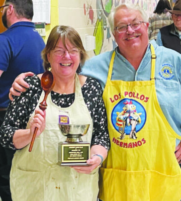 Two winners of a cooking competition pose together as they hold their trophies.