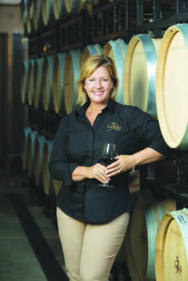 Amy LaBelle poses for a photo by a wall of wine barrels