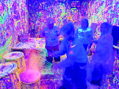 people wearing protective gear in black lit room with neon paint spatters