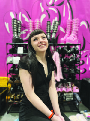 young woman sitting in front of wire shelves filled with black and pink platform shoes