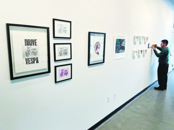 A young man takes pictures of pictures on display in an art gallery.