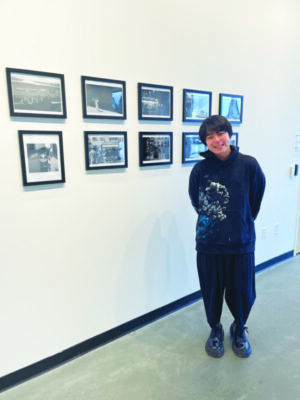 A student poses with a series of pictures on display in an art gallery.