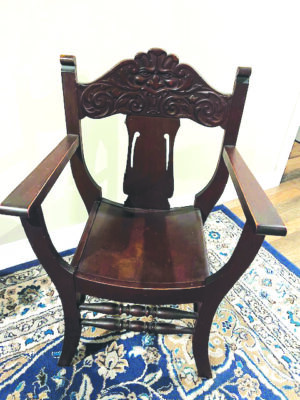 wooden chair with curved seat and high armrests, carving on back showing angry looking face of wind spirit