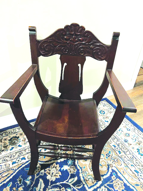 wooden chair with curved seat and high armrests, carving on back showing angry looking face of wind spirit