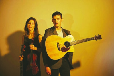 Two band players stand side by side in a dramatic photo with yellow lighting