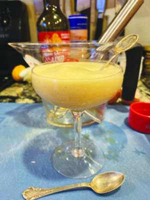 frothy light yellow custard in a margarita glass with spoon, sitting on kitchen counter