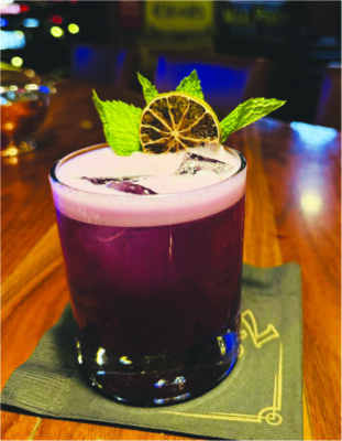 A purple cocktail drink with a pretty leaf decoration