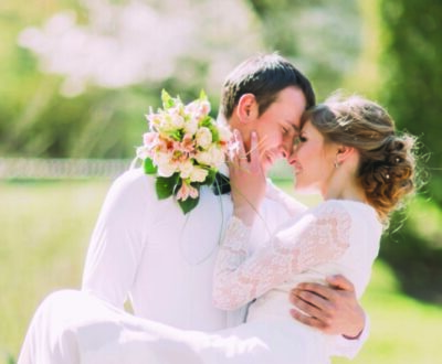 Groom carrying his beautiful bride on arms leaning foreheads at spring park.