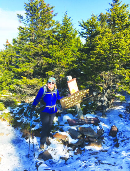 A woman hiking in winter poses next to a state park sign.