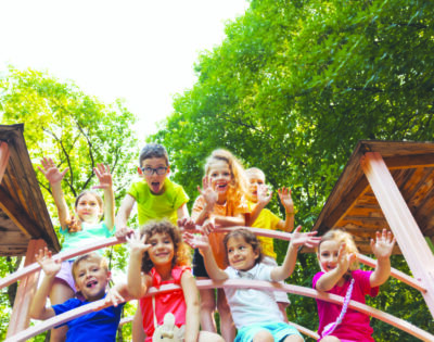 View from low angle of little kids who are sitting on a bridge in the playground. The happy kids spend time together in the summer park