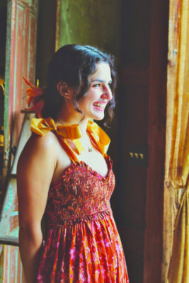 A photo of Ashley Place, wearing an orange dress and smiling