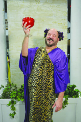 A theater actor dressed in Greek garb holding up an apple.