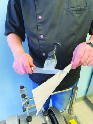 A man uses a freshly sharpened knife to cut through a piece of paper.