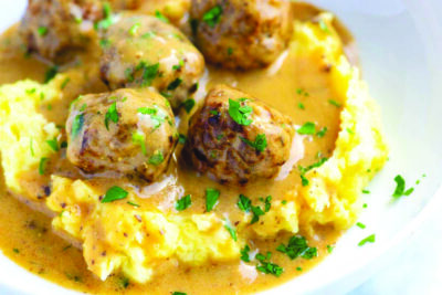 A plate of Swedish meatballs, sitting in a pool of gravy surrounded by mashed potatoes