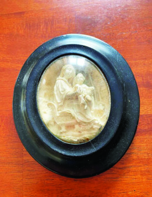 small carved relief of the Virgin Mary and baby Jesus, made of clay, encased in black round frame under glass