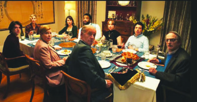 film still from Bad Shabbos showing a group of people sitting around a dinner table, looking in the direction of the camera