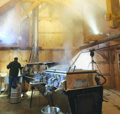 A man goes about his work boiling off water to make maple syrup.