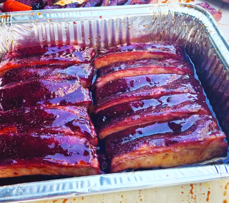 rectangular aluminum baking dish filled with cut ribs glazed in a shiny maple sauce, close up