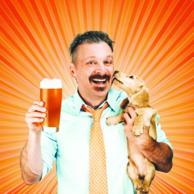 man with mustache, wearing button up shirt and bright tie, holding beer in one hand and puppy in the other, orange burst background