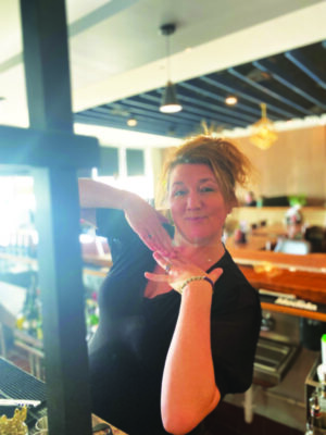 woman wearing black shirt, posing behind bar at restaurant, sunlight coming in through window