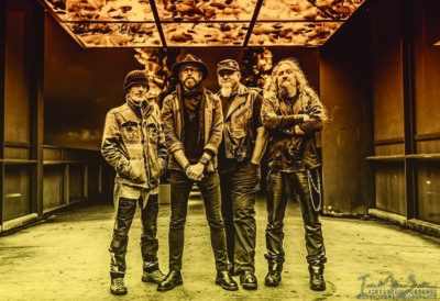 four male band members standing in large empty room, photo in sepia tones
