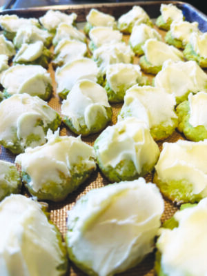 rows of small cookies covered in frosting sitting on baking sheet