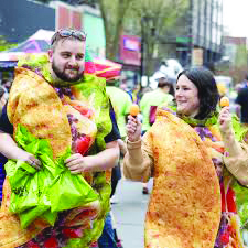 man and woman dressed as tacos as they walk down the street during community event