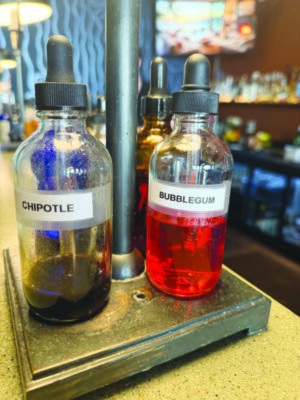 two eyedropper bottles, one labelled chipotle, one labelled bubble gum, sitting on bar top, partially full of colored liquid