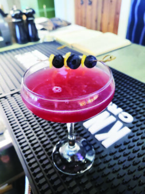 A blueberry Daiquiri, sitting in a wide top glass ornamented with a fruit spear.