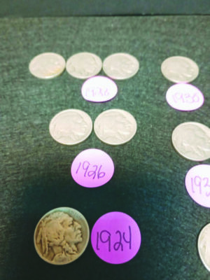 old coins laid out on dark paper, pieces of round paper beside them with dates