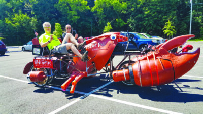A giant lobster-bike made out of random parts and pieces, piloted by two men.