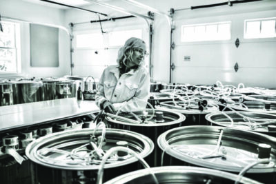 black and white image of a woman standing in room full of barrels, light streaming in from small windows