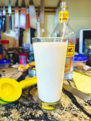 glass of light colored drink on counter with bottle of gin and lemon squeezer