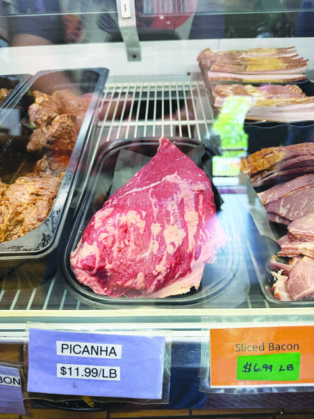 round-ish hunk of uncooked meat with striations of fat, sitting on shelf in refrigerated retail case
