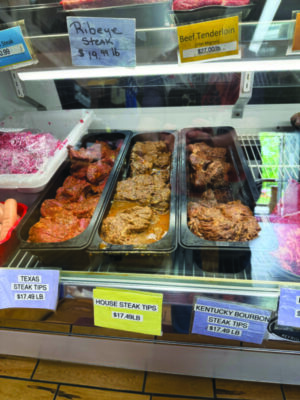 three long containers of three different flavors of steak tips, filled with marinade, in refrigerated case at marketplace